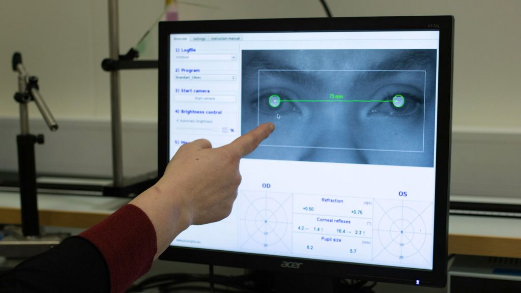 En hånd peker på en dataskjerm med bilde av to øyne.